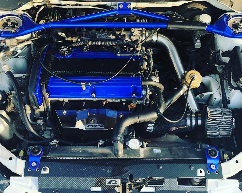 Modified Mitsubishi Evo engine bay with blue valve cover and strut bar