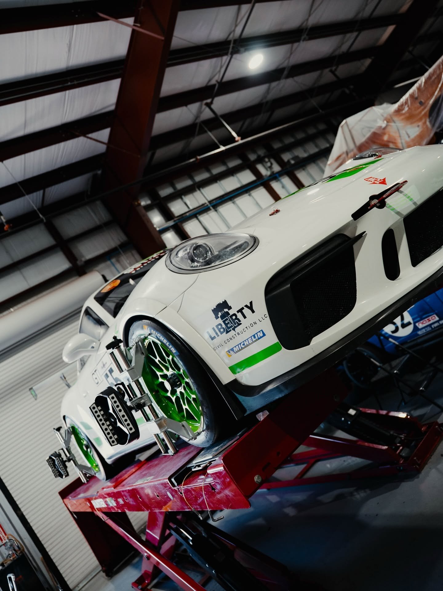 White GT3 Cup race car with green wheels on the alignment rack