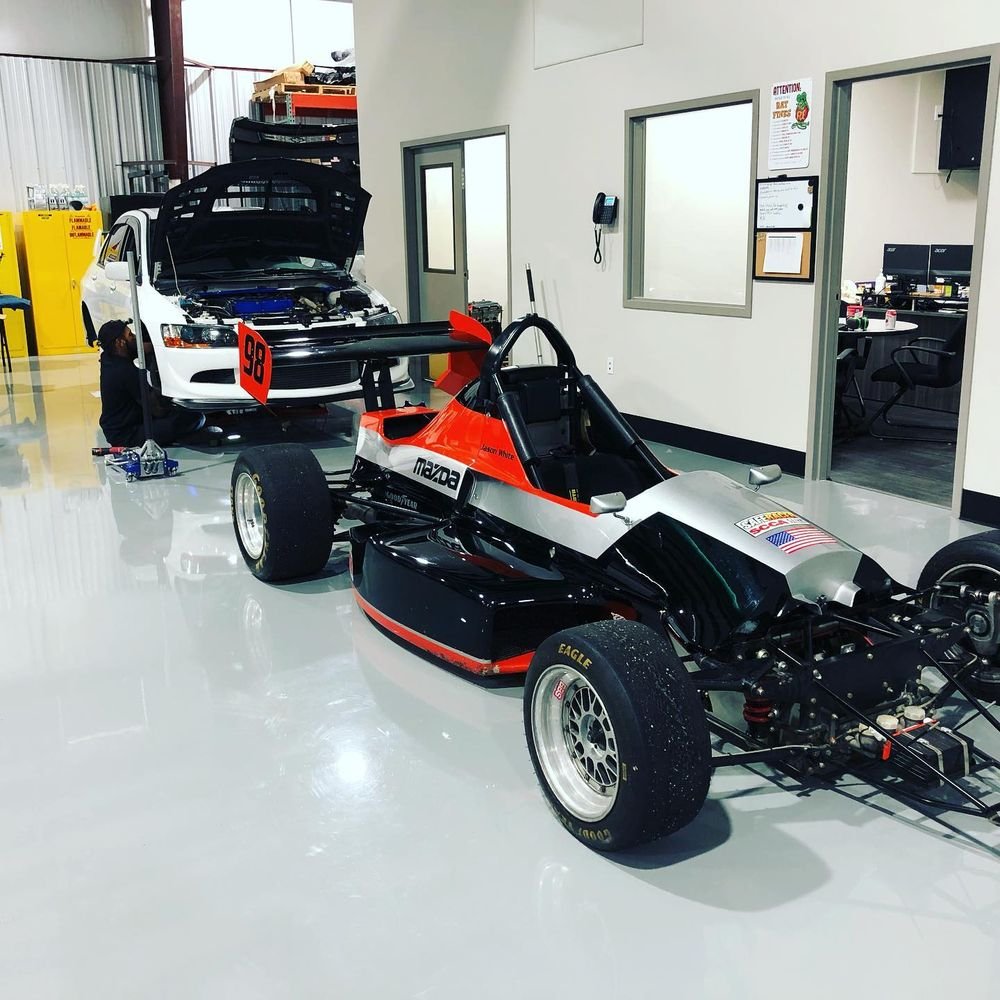 Formula-style race car prepped in the shop next to a customer car getting track-day work